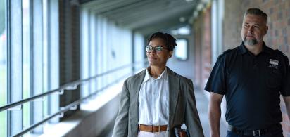 Zwei Personen gehen durch einen Flur, eine trägt ein Namensschild mit 