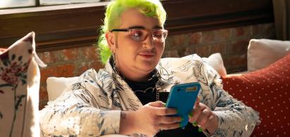 A genderqueer person looking at their phone