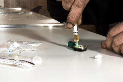 Person sitzt an einem Tisch und bereitet eine Spritze zum Drogenkonsum vor