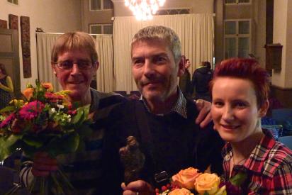 Drei der Preisträger mit Preisstatue und Blumen stehen unter einem Kronleuchter