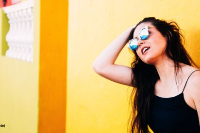 Frau mit Sonnenbrille lehnt an gelber Wand