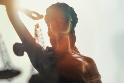 Justitia-Statue mit verbundenen Augen und einer Waage in der rechten Hand im Gegenlicht