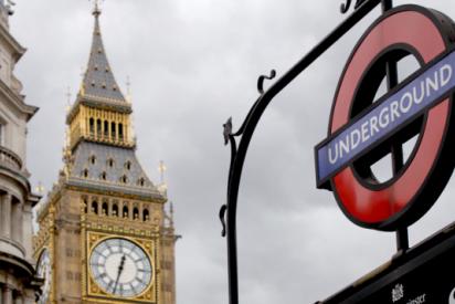 Im Vordergrund ist das Schild zu einem Eingang der Londoner U-Bahn mit der Beschriftung "Underground" zu sehen. Im Hintergrund sieht man den oberen Teil des Turms der Houses of Parliament mit der Uhr von Big Ben.