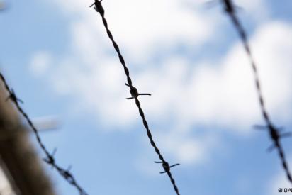 Stacheldraht an einem Gebäude von unten vor blauem Himmel mit weißen Wolken fotografiert